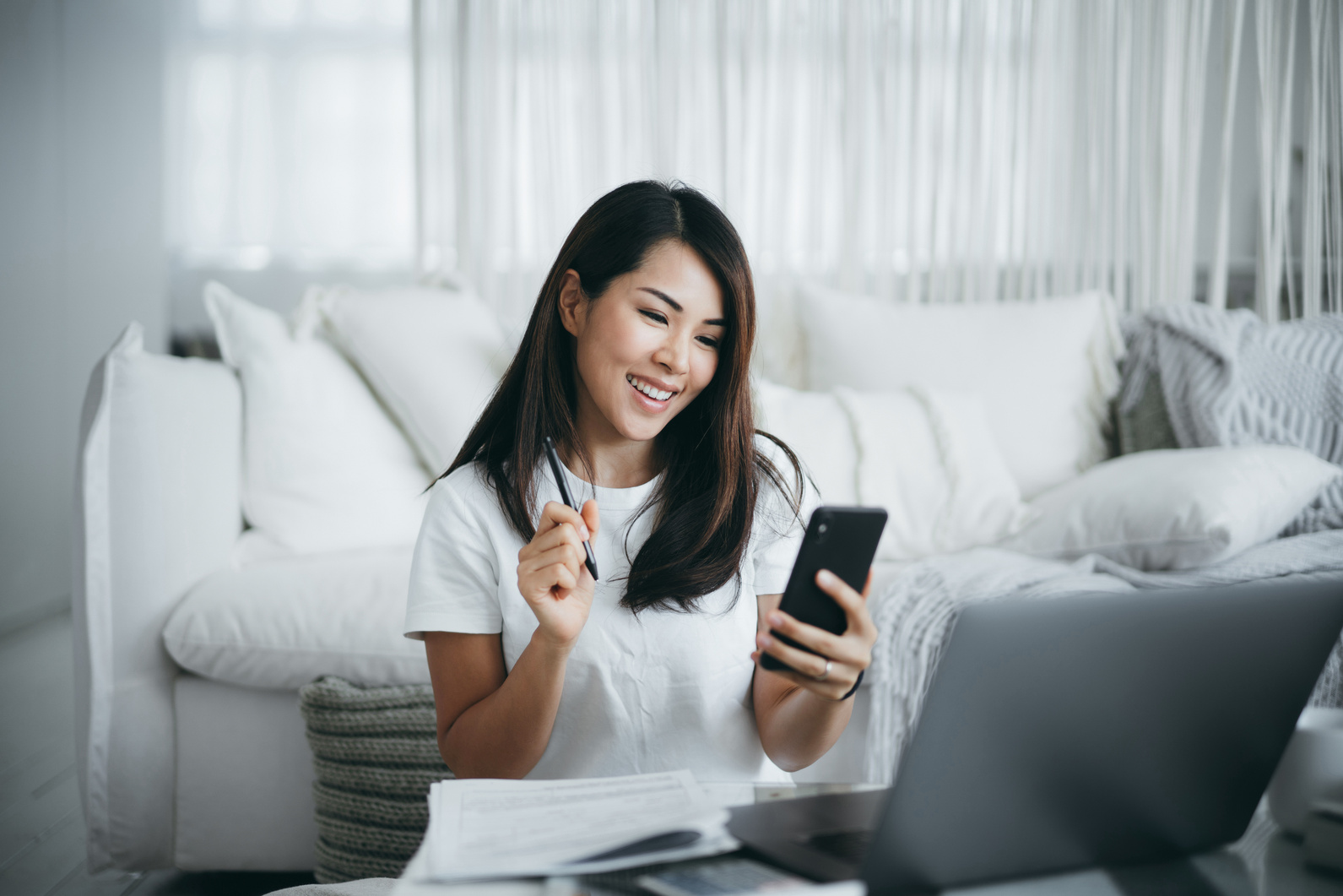 Young Asian woman sitting on the floor in the living room working from home using laptop computer and handling paperworks